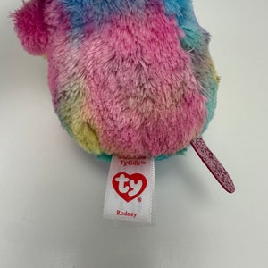May include: A rainbow tie-dye plush toy with a red tail. The toy has a TySilk tag with the Ty logo and the name Rodney.