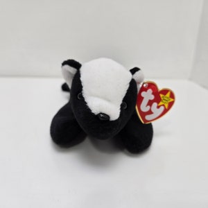 May include: Black and white beanie baby plush toy shaped like a skunk. The toy has a red heart-shaped tag with the word "ty" on it.