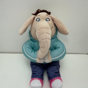 May include: A plush elephant toy wearing a teal hoodie with white trim, blue jeans, and pink-soled sneakers. The elephant has large ears, a long trunk, and brown hair. The toy is standing against a white background.