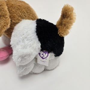 May include: A brown and white plush dog toy with black markings. The toy has a Ty tag that says "Cookie".
