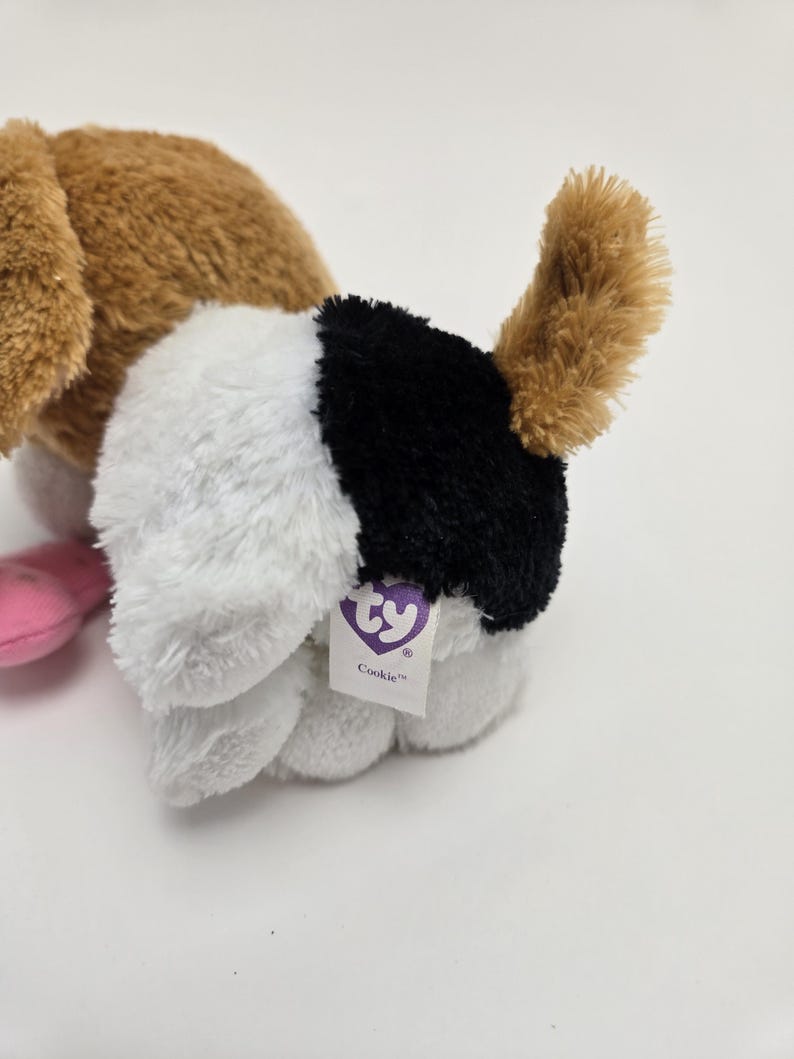 May include: A brown and white plush dog toy with black markings. The toy has a Ty tag that says "Cookie".
