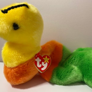 Op de afbeelding: Een gele, oranje, groene en blauwe pluche slang met een zwarte streep op zijn kop. De slang heeft een rood Ty Beanie Baby-label aan zijn zijde bevestigd. Het label heeft een witte ster en het woord "Ty" in wit.