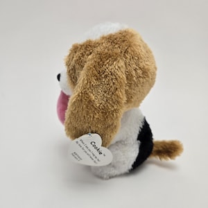 May include: A brown and white plush dog toy with black accents. The toy has a pink tongue sticking out and a tag that reads "Cookie" with the text "What I love most, I miss so dear. My love for you, will never disappear!"