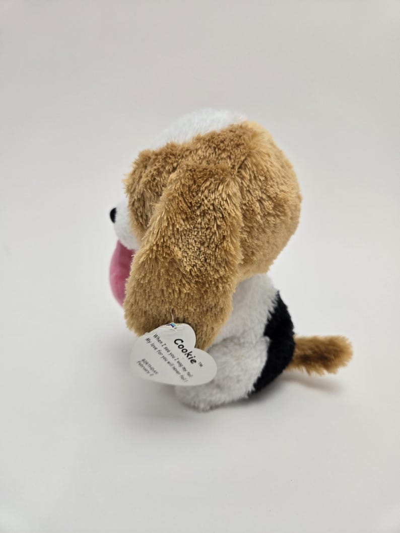 May include: A brown and white plush dog toy with black accents. The toy has a pink tongue sticking out and a tag that reads "Cookie" with the text "What I love most, I miss so dear. My love for you, will never disappear!"