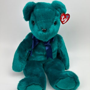 May include: A teal green plush teddy bear with a navy blue ribbon around its neck. The bear has a Ty tag attached to its ear.