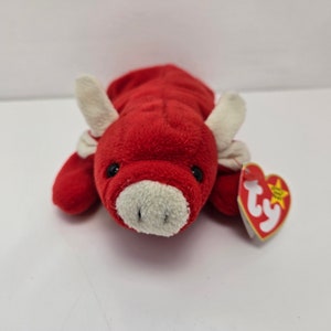 以下が含まれることがあります： 赤いと白いぬいぐるみのおもちゃの雄牛。Tyのタグには星付きで「Ty」と書いてあります。