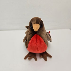 May include: A brown and red plush robin bird toy with a white belly and a brown beak. The toy has a red breast and is sitting on a white surface.