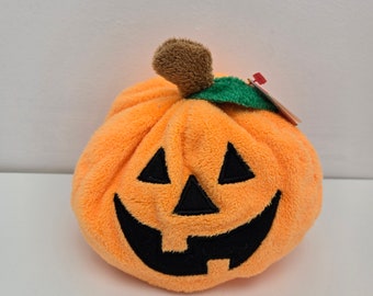 Puede incluir: Calabaza de felpa naranja con una cara de calabaza tallada negra. La calabaza tiene un tallo verde y una parte superior marrón y peluda.