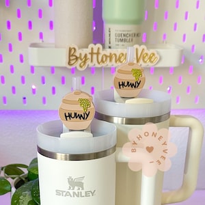 May include: Two white stainless steel tumblers with lids. The lids have a honey pot charm with the word "Huny" on them. The tumblers are decorated with a pink and gold sticker that says "By Honey Vee".