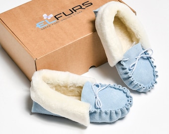 May include: A pair of light blue suede moccasins with white shearling lining. The moccasins are in a box with the text "El Furs Greek Furs Online Store" printed on the top.