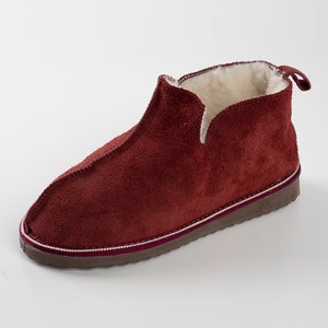 May include: Burgundy suede slippers with a white fleece lining and a brown rubber sole.
