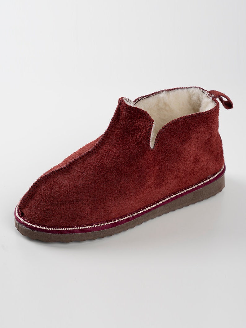 May include: Burgundy suede slippers with a white fleece lining and a brown rubber sole.