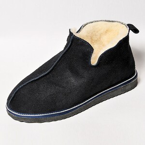 May include: Black suede slippers with a white and blue trim. The slippers have a shearling lining.
