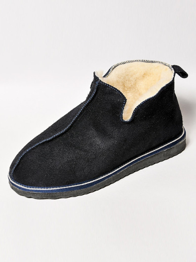 May include: Black suede slippers with a white and blue trim. The slippers have a shearling lining.
