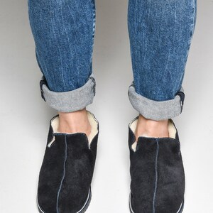 May include: A pair of black suede slippers with a white shearling lining. The slippers have a navy blue trim around the sole.
