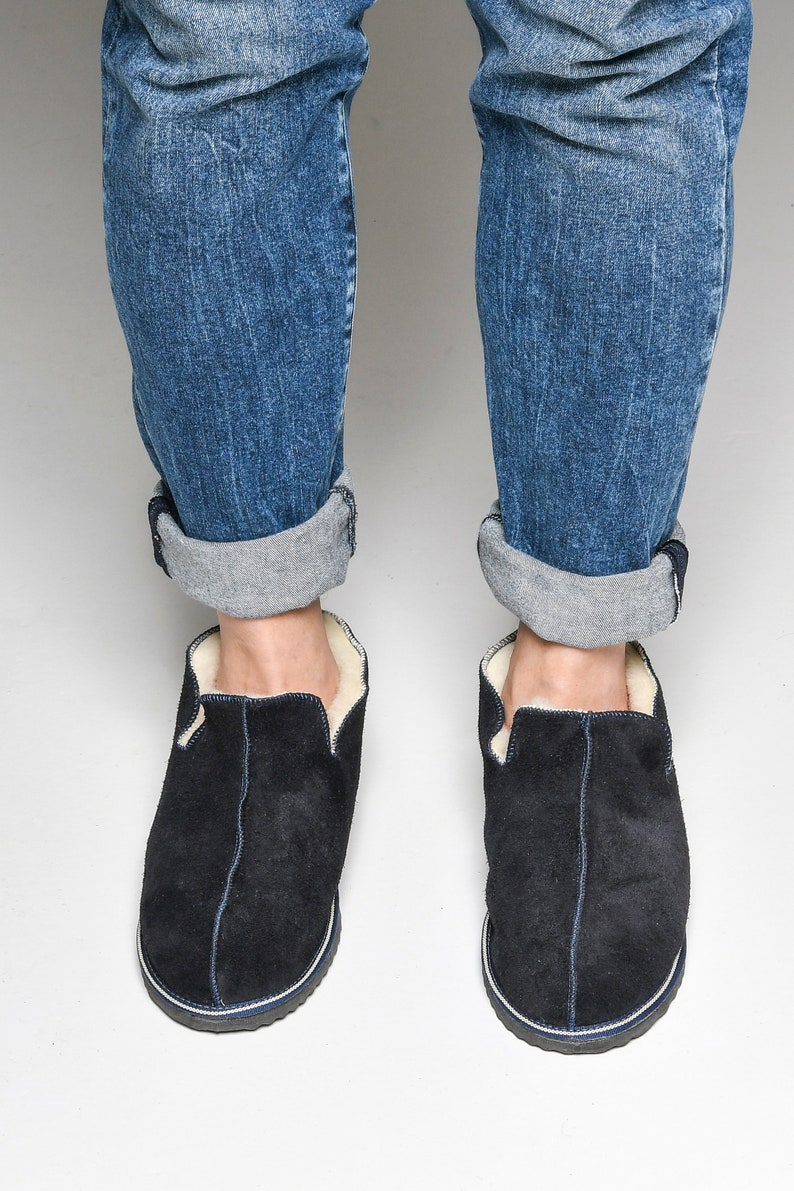 May include: A pair of black suede slippers with a white shearling lining. The slippers have a navy blue trim around the sole.