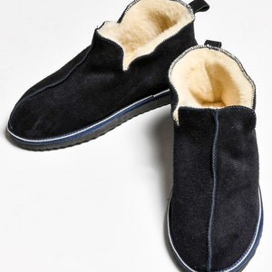May include: A pair of black suede slippers with a white and blue trim. The slippers have a soft, fuzzy lining.