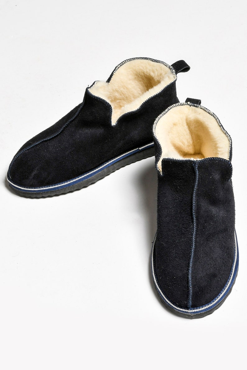 May include: A pair of black suede slippers with a white and blue trim. The slippers have a soft, fuzzy lining.