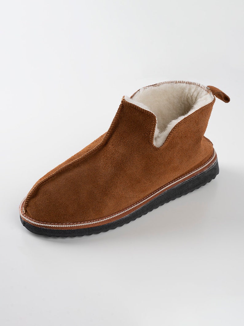 May include: Brown suede slippers with a shearling lining and a black rubber sole.