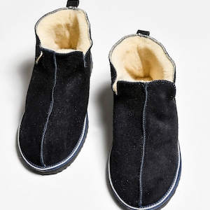 May include: A pair of dark blue suede slippers with a white trim and a sheepskin lining.