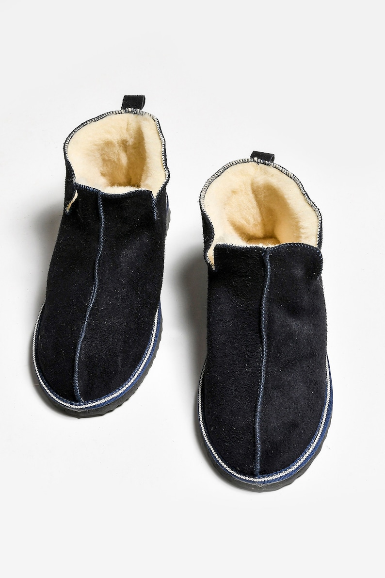 May include: A pair of dark blue suede slippers with a white trim and a sheepskin lining.