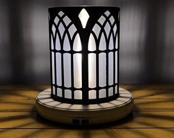 May include: A black metal lamp with a white frosted glass shade. The shade has a gothic arch design. The lamp is on a white base with a power cord.