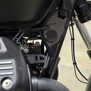 Könnte beinhalten: Nahaufnahme eines schwarzen Motorradrahmens mit verschiedenen sichtbaren Komponenten. Das Bild zeigt den Motor, den Rahmen und die Vorderradaufhängung. Das Motorrad hat eine mattschwarze Oberfläche mit einer runden schwarzen Abdeckung am Rahmen.