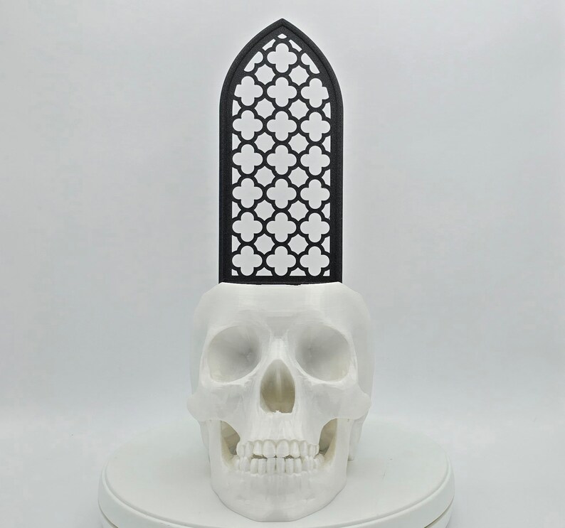 May include: A white skull planter with a black geometric design on top. The planter is made of ceramic and has a smooth finish.