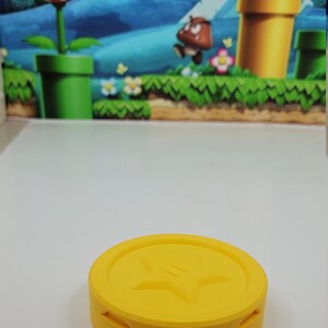 May include: A yellow plastic coin with a star design on the top. The coin is a collectible item for video game fans.
