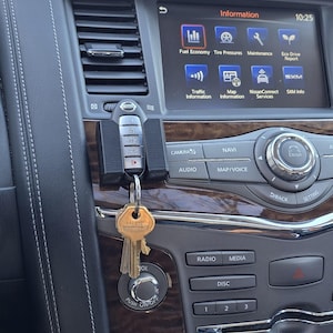 May include: A close-up of a car's dashboard with a key fob hanging from the keyhole. The dashboard features a touchscreen display with the words "Information" and "10:25" displayed. The display also shows icons for fuel economy, tyre pressure, maintenance, and eco drive report. Below the display are buttons for camera, audio, navi, map/voice, radio, media, disc, and climate control.