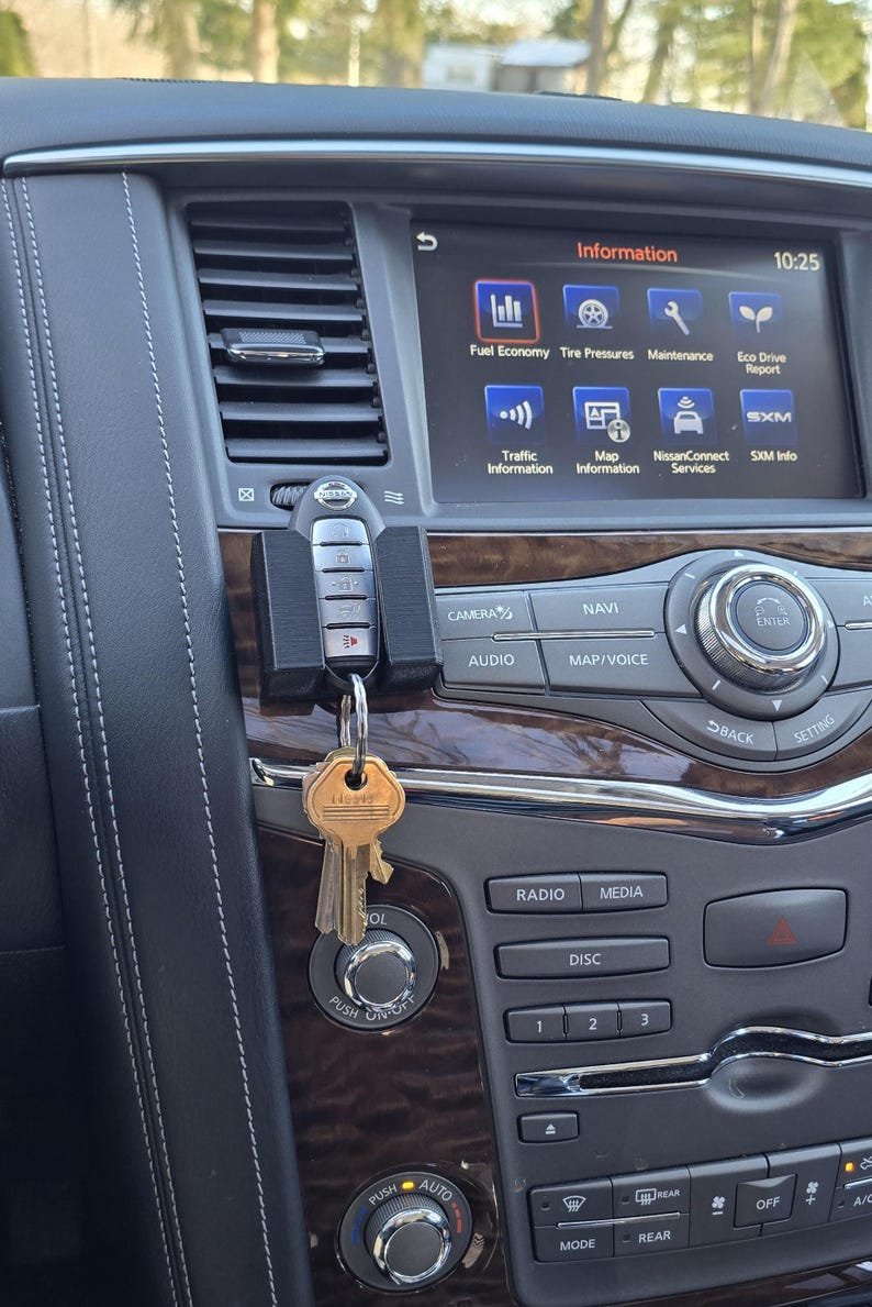 May include: A close-up of a car's dashboard with a key fob hanging from the keyhole. The dashboard features a touchscreen display with the words "Information" and "10:25" displayed. The display also shows icons for fuel economy, tyre pressure, maintenance, and eco drive report. Below the display are buttons for camera, audio, navi, map/voice, radio, media, disc, and climate control.