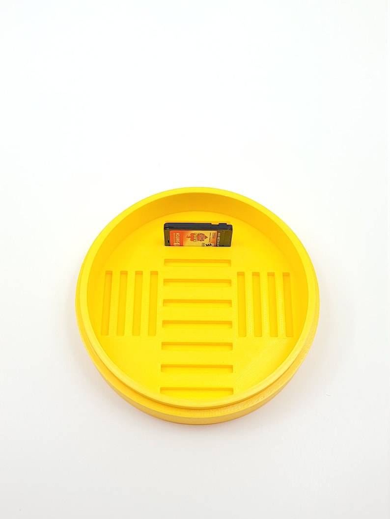 May include: A yellow plastic container with a grid pattern on the inside. A game cartridge is sitting inside the container.