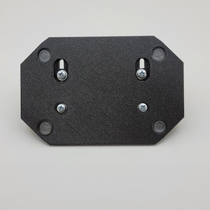 May include: A black, octagonal mounting plate with a textured surface. It features two screws and four small, circular magnets. The plate is designed for mounting and is shown against a white background.