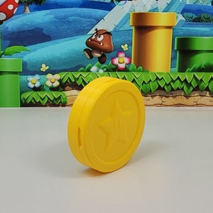 May include: A yellow plastic coin with a five-pointed star in the center. The coin is a prop for a video game.