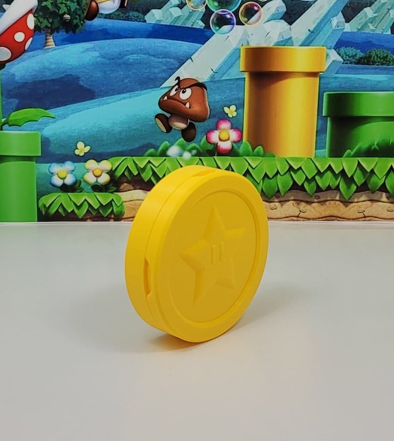 May include: A yellow plastic coin with a five-pointed star in the center. The coin is a prop for a video game.