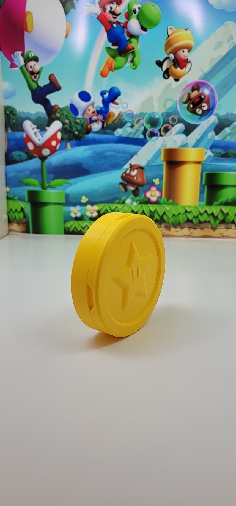 May include: A yellow plastic coin with a star and a small figure inside. The coin is a collectible item for fans of the Super Mario video game series.
