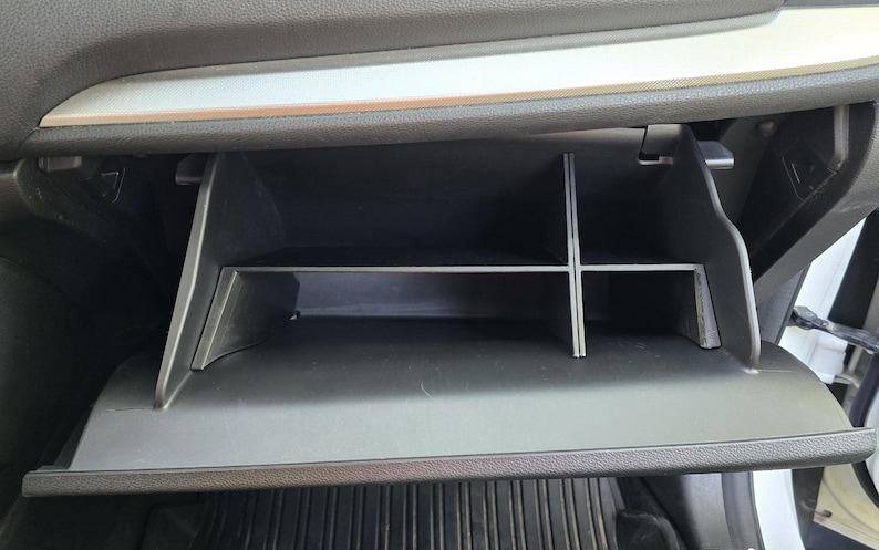 K&ouml;nnte beinhalten: Ge&ouml;ffnete schwarze Auto-Handschuhfach mit silberner Zierleiste. Das Fach ist in Abschnitte mit einem Regal unterteilt. Der Innenraum ist schwarz mit einer strukturierten Oberfl&auml;che.