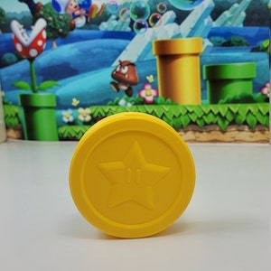 May include: A yellow plastic coin with a five-pointed star and two small circles in the center. The coin is a replica of a Super Mario Bros. power-up.