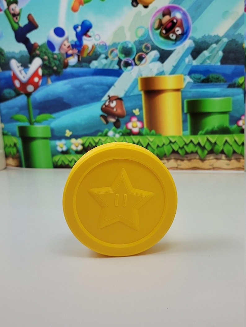 May include: A yellow plastic coin with a five-pointed star and two small circles in the center. The coin is a replica of a Super Mario Bros. power-up.