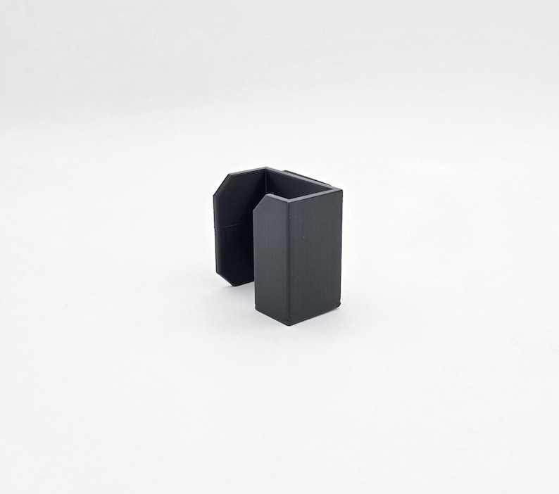 May include: A matte black, U-shaped desk organizer. The organizer has a rectangular base and two upright sections, creating a space for holding items. The design is simple and modern, suitable for office or home use.
