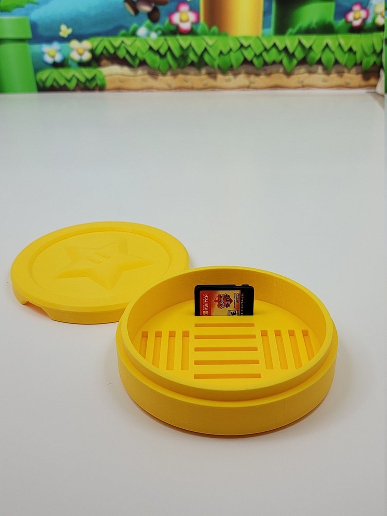 May include: Yellow plastic case with a lid and a game cartridge inside. The case has a star design on the lid and a grid pattern on the bottom. The game cartridge is for the Nintendo Switch.