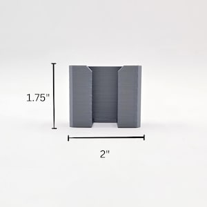 May include: A grey plastic phone stand, measuring 5 cm wide and 4.5 cm tall.