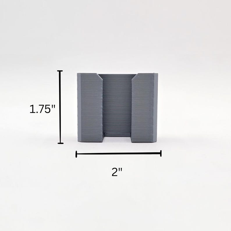 May include: A grey plastic phone stand, measuring 5 cm wide and 4.5 cm tall.