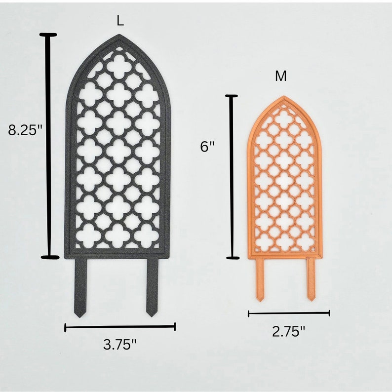 May include: Two decorative metal garden trellises, one black and one orange. The larger trellis is 8.25 inches tall and 3.75 inches wide. The smaller trellis is 6 inches tall and 2.75 inches wide. Both trellises have a gothic arch design with a lattice pattern.