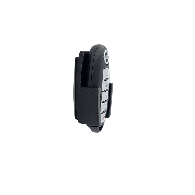 May include: A black plastic key holder with a gray Nissan car key inside. The key holder has a clip on the back for attaching to a belt or bag.