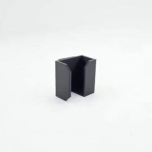 May include: A black, open-sided, rectangular container with a squared-off design. The container has a matte finish and is set against a white background. The object appears to be a holder or organizer.