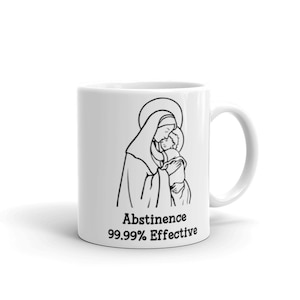 Könnte beinhalten: Weiße Keramiktasse mit einer schwarzen Strichzeichnung der Jungfrau Maria, die das Jesuskind hält. Der Text "Abstinenz 99,99 % effektiv" ist unter dem Bild gedruckt.