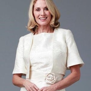 May include: A white bolero jacket with a floral pattern and short sleeves. The jacket has a simple design and a slightly fitted silhouette.