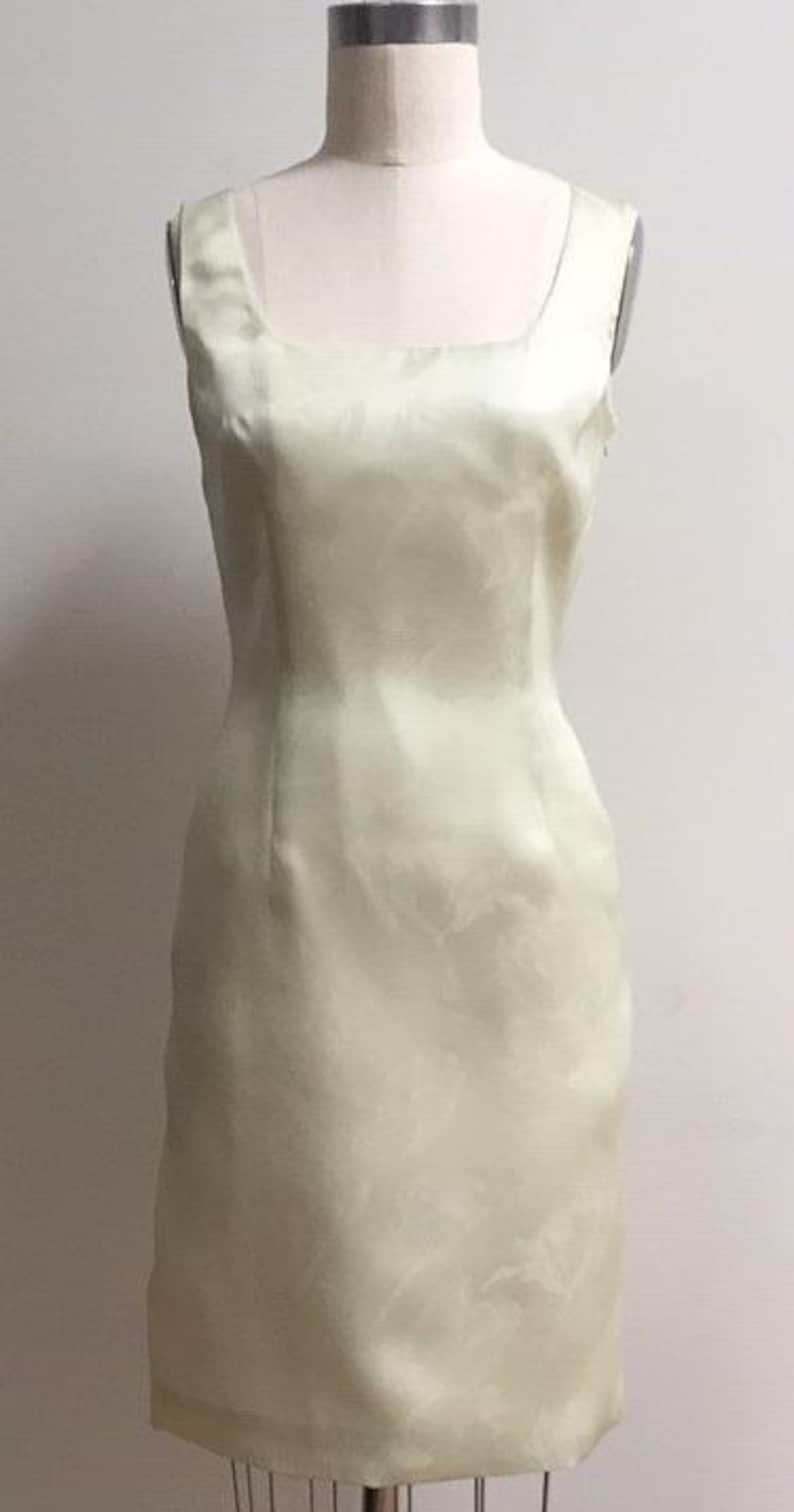 Puede incluir: Un vestido sin mangas de color amarillo claro con un escote cuadrado. El vestido est&aacute; hecho de una tela sedosa y tiene una silueta ajustada.