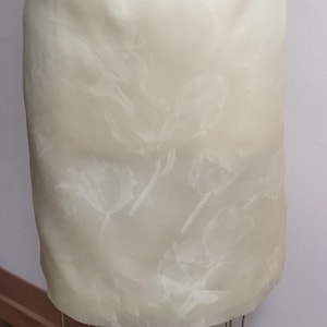 Puede incluir: Una falda blanca con un sutil estampado floral en relieve. La falda est&aacute; hecha de una tela ligera y tiene una textura suave y sedosa.